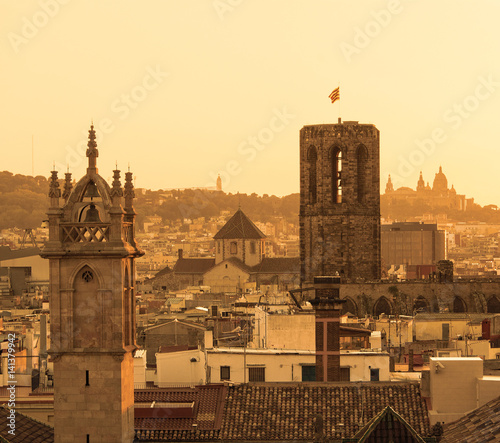 Top view of the old quarter of Barcelona with a tower with catalan flag on the flagpole in the foreground at sunset.