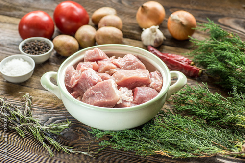 Raw pork ham with vegetables and spices on a wooden cutting board
