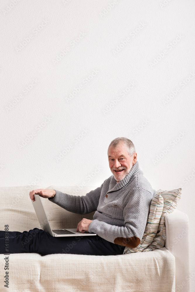 Senior man sitting on sofa, working on laptop.