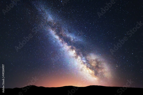 Milky Way. Fantastic night landscape with bright milky way, sky full of stars, yellow city light and mountains. Picturesque scene with our universe. Space background. Amazing astrophotography