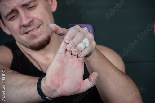 Close up portrait of suffering climber man that trying to stretch fingers. Sportsman feel pain after exercising in climbing gym.
