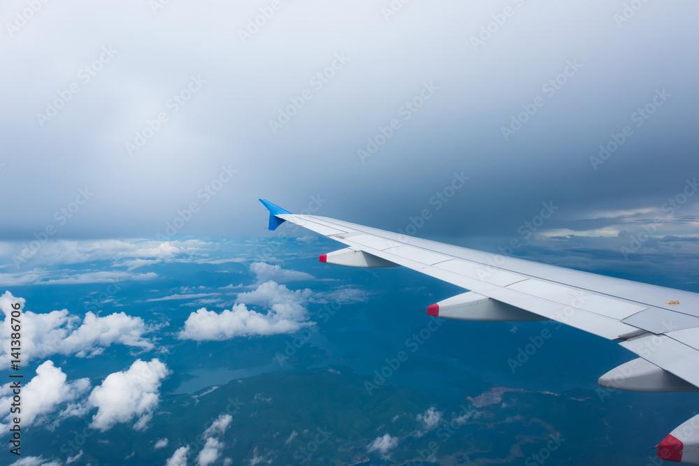 Wing of an airplane flying above the mountain and clouds