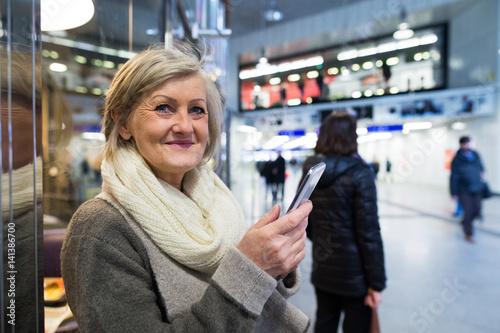 Photography Senior woman with smartphone in hallway of subway