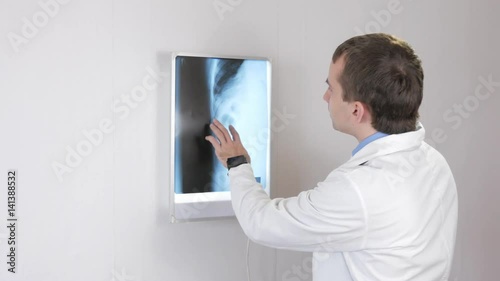 The doctor examines the X-ray and drinks a hot drink. White wall and Nigatoscope with ribs and thorax photo