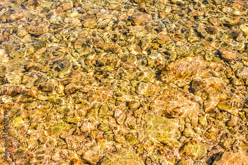 Kamienie w wodzie. Kamienista plaża. Kolorowe refleksy na wodzie.