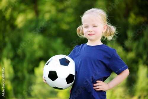 Cute little soccer player having fun playing a soccer game on summer day