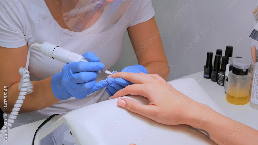 The master uses an electric machine to remove the nail polish on client hands during hardware manicure in the salon. Beauty and nail care concept