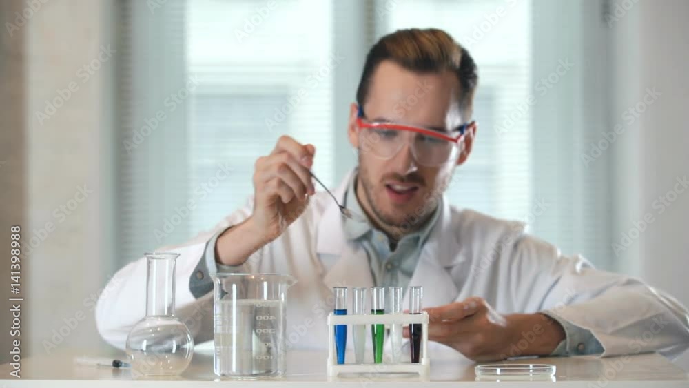 a chemist pours white parascale in a test tube. he is dressed in a white coat and goggles. a chemist pours white parascale in a test tube. he is dressed in a white coat and goggles.