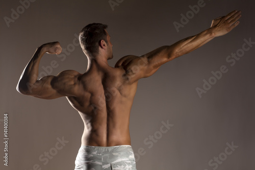 rear view of the half-naked handsome and muscular young man posing on a gray background