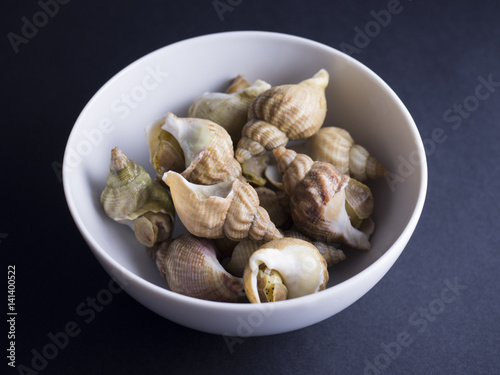 Whelks (sea snails) in white bowl isolated on black background
