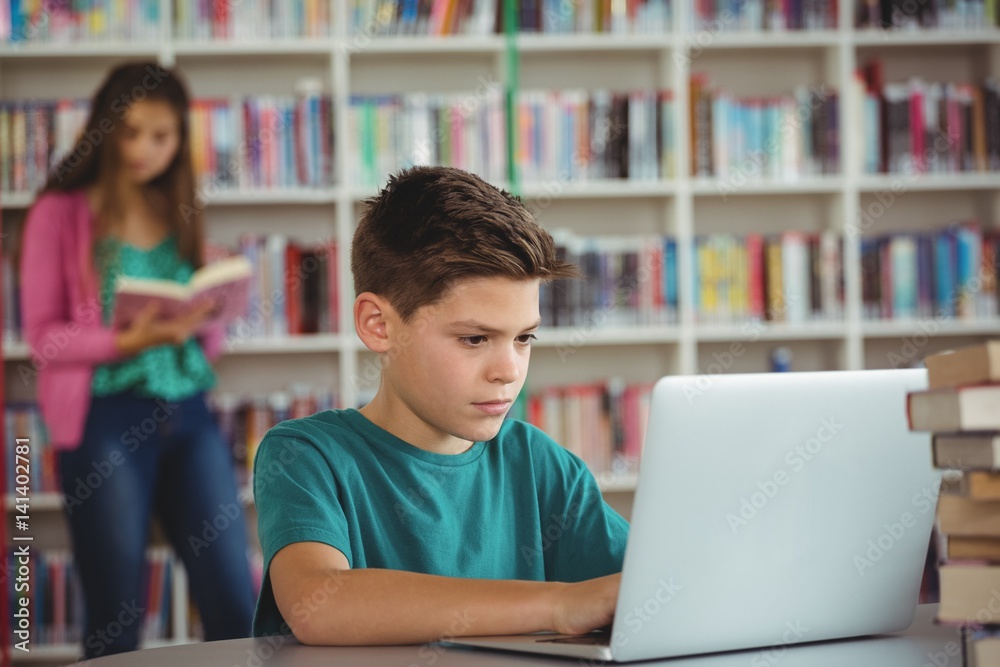 Schoolboy using laptop in library at school Schoolboy using laptop in library at school