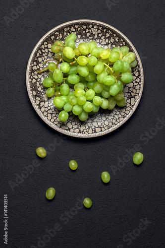 Fresh green grapes in a clay bowl closeup on a black background