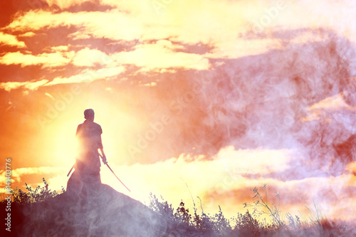 Fotografie Silhouette of a warrior with a sword in the smoke of a mountain war