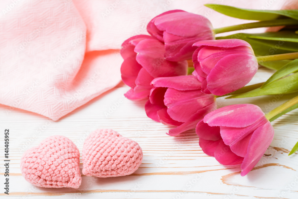 Пара вязанных розовых сердец и букет свежих тюльпанов на деревянном столе