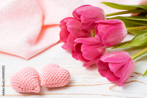 Пара вязанных розовых сердец и букет свежих тюльпанов на деревянном столе