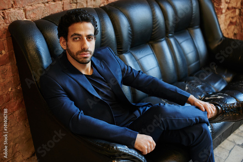 Portrait of Arab man in a suit sitting on leather sofa in black colour