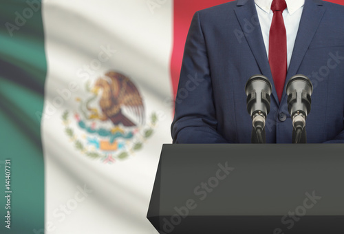Businessman or politician making speech from behind a pulpit with national flag on background - Mexico photo
