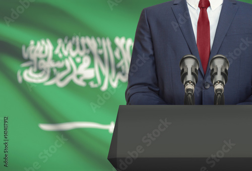 Businessman or politician making speech from behind a pulpit with national flag on background - Saudi Arabia
