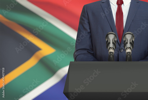 Businessman or politician making speech from behind a pulpit with national flag on background - South Africa
