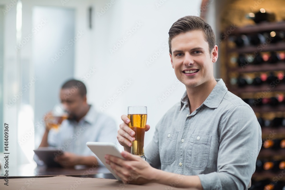 Handsome man holding beer glass while using digital tablet