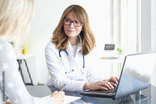 Doctor and her patient. Shot of a middle aged female doctor sitting in front of laptop and consulting with her patient.