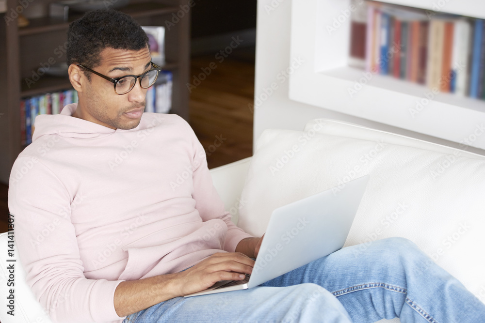 Browsing on the internet. full length shot of a smiling young afro American man using a laptop while relaxing in his living room at home. Browsing on the internet. full length shot of a smiling young afro American man using a laptop while relaxing in his living room at home.
