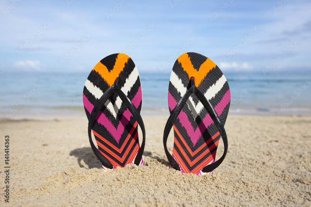 Colorful flip-flops stuck in the sand on tropical beach with turquoise ocean in the background Colorful flip-flops stuck in the sand on tropical beach with turquoise ocean in the background