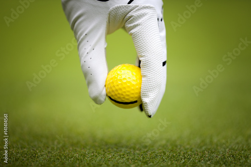 Man's hand in a white glove putting a golf ball in a golf course