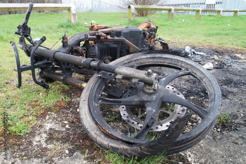 Burnt down motorbike on the green grass.