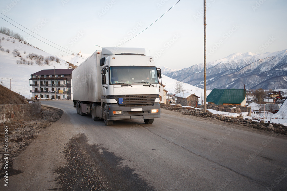 Obraz premium White refrigerated truck on winter road on background of the mountains