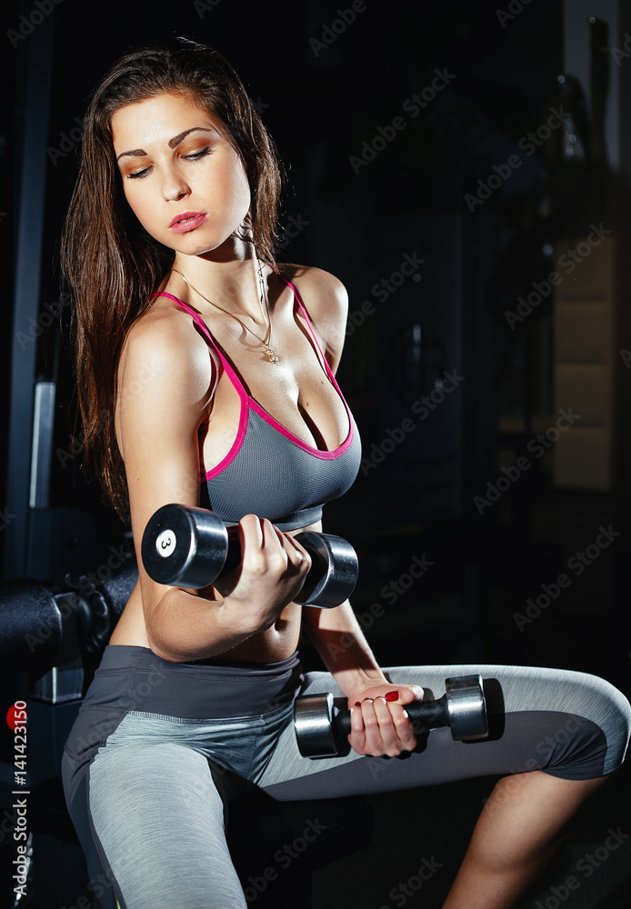 Young beautiful girl with big breasts and good figure in sports hall with  dumbbells in hands Stock Photo