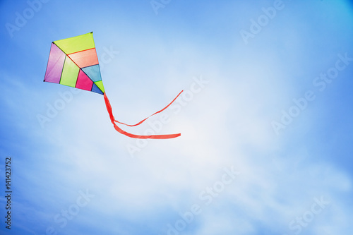 angle view of a colorful kite flying with waving red bow in a deep blue sky with the light of the sun photo