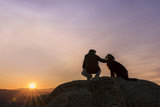 Man and his faithful companion watching the sunrise on top of the mountain