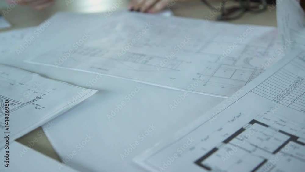 Close up papers with design drawings on meeting inside office. Managers of three workers discussing business project. Closeup shooting of hands watching on paper. Drafts for construction of large