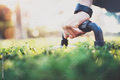 Healthy lifestyle concept.Closeup view of male hand while doing pushups in the park on the sunny morning.Training outdoors.Fit shirtless male fitness model in crossfit exercise outdoors.Blurred.