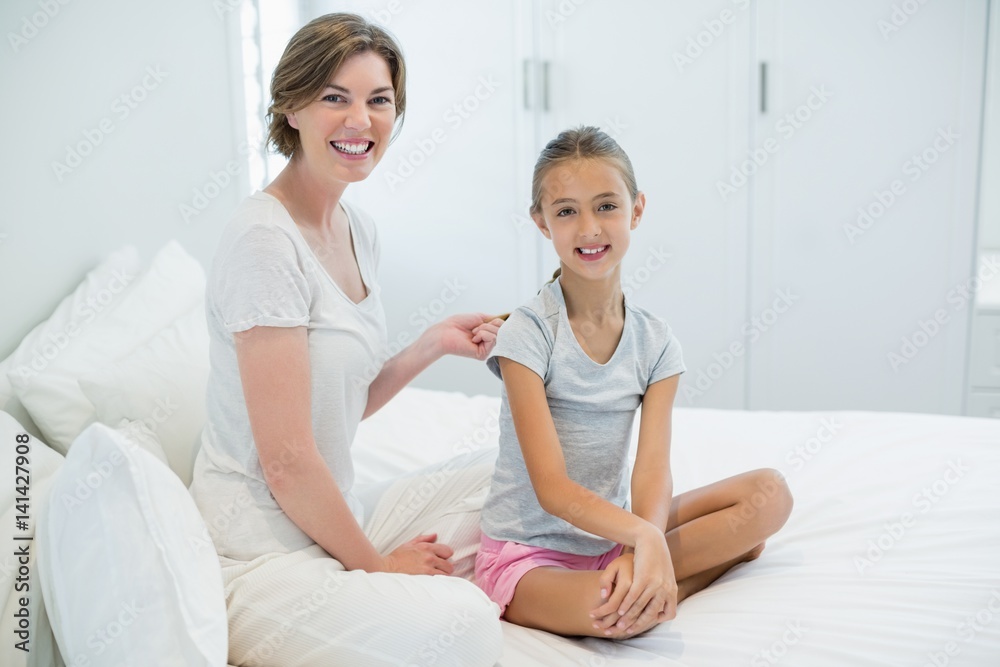 Smiling mother combing daughters hair on bed in bedroom at home Smiling mother combing daughters hair on bed in bedroom at home