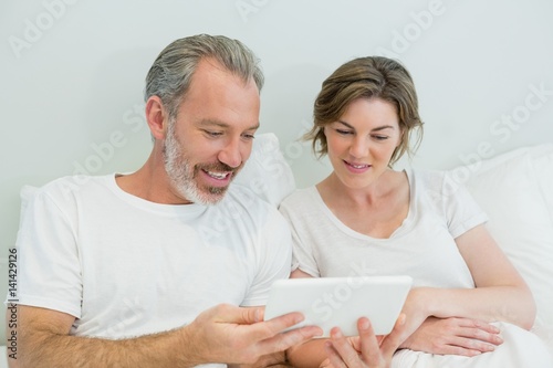 Smiling couple using digital tablet on bed in bedroom