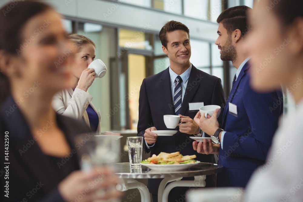 Businesspeople interacting with each other while having coffee - obrazy, fototapety, plakaty 