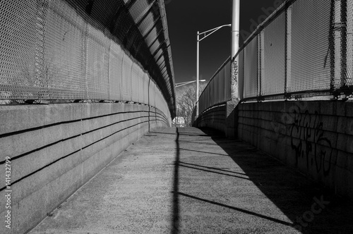 Urban chain link fence walkway. Industrial art and design. Overpass concrete bridge walkway.Black and white. Abstract art and design. Outdoor architectural detail and design. Abstract colors. 
