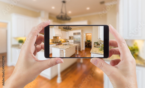Female Hands Holding Smart Phone Displaying Photo of Kitchen Behind. photo