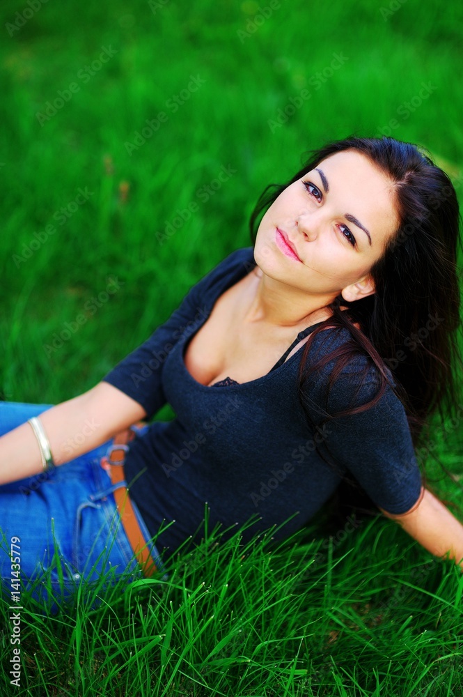 Portrait of young pretty woman brunette with beautiful brown eyes in a dark blouse with a deep cleavage, relaxed on green grass in a Park, closeup. Portrait of young pretty woman brunette with beautiful brown eyes in a dark blouse with a deep cleavage, relaxed on green grass in a Park, closeup.