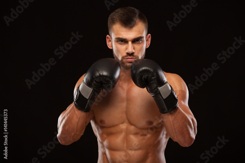 Muscular young man with perfect Torso with six pack abs, in boxing gloves is showing the different movements and strikes isolated on black background with copyspace © satyrenko