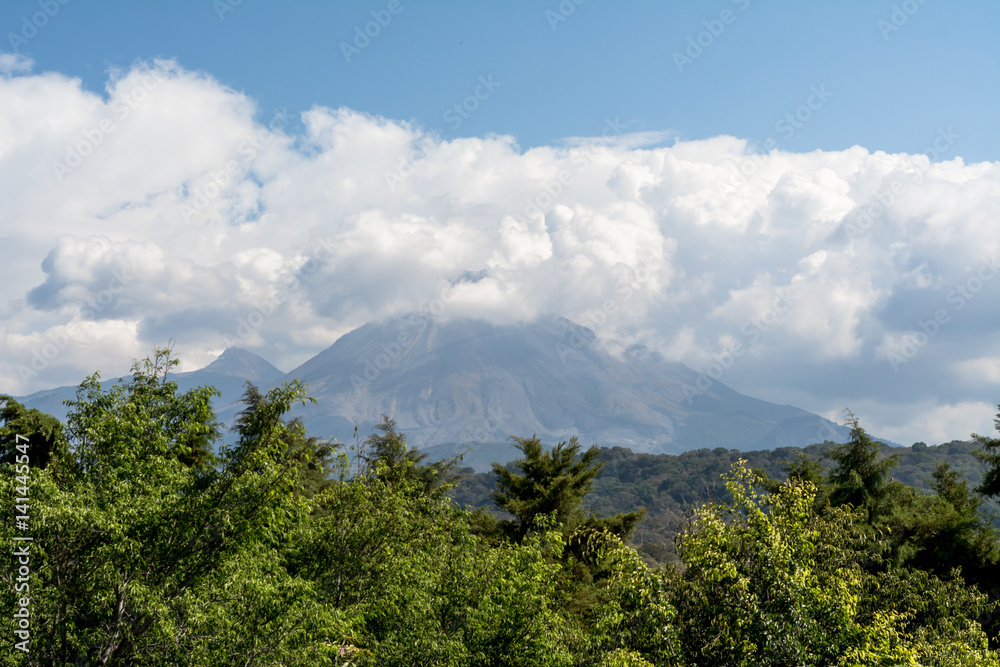 El volcán de Colima está cubierto por nubes y plantas verdes.
