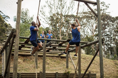 Fit men climbing down the rope during obstacle course
