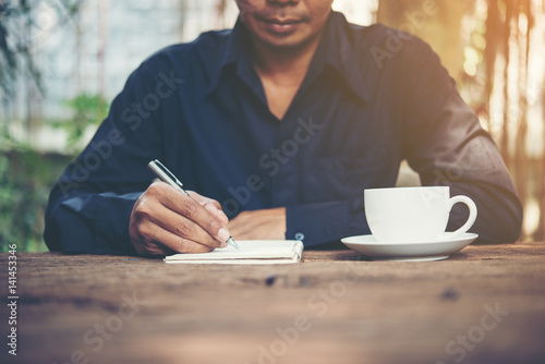 Young man writing on a notebook working on a rustic wooden table.