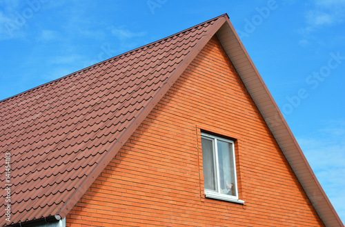 Red metal sheets house roof tiles. Metal Roof Shingles - Roofing Construction, Attic Exterior, Roofing Repair. Brick House.