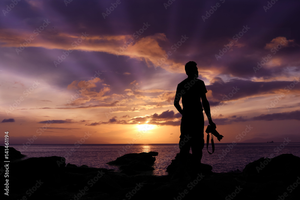 Silhouette photographer standing on the rocks by the sea with purple sky sunrise in the morning. 