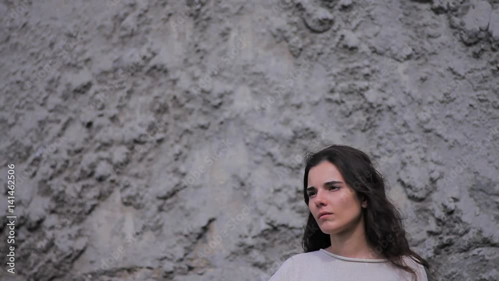 Slow Motion Side View Sad Lonely Brunette Stands Against a Gray Stone Wall and Looks Out Into the Distance Slow Motion Side View Sad Lonely Brunette Stands Against a Gray Stone Wall and Looks Out Into the Distance