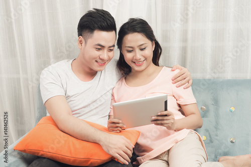Couple at home relaxing on sofa with digital tablet