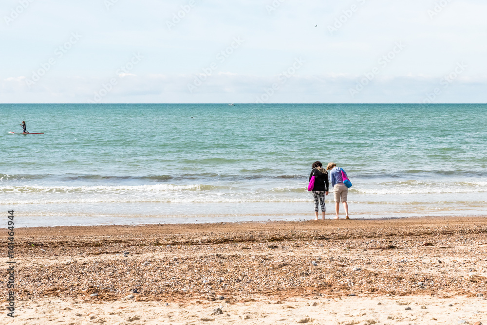 Two women trying sea water on sand beach